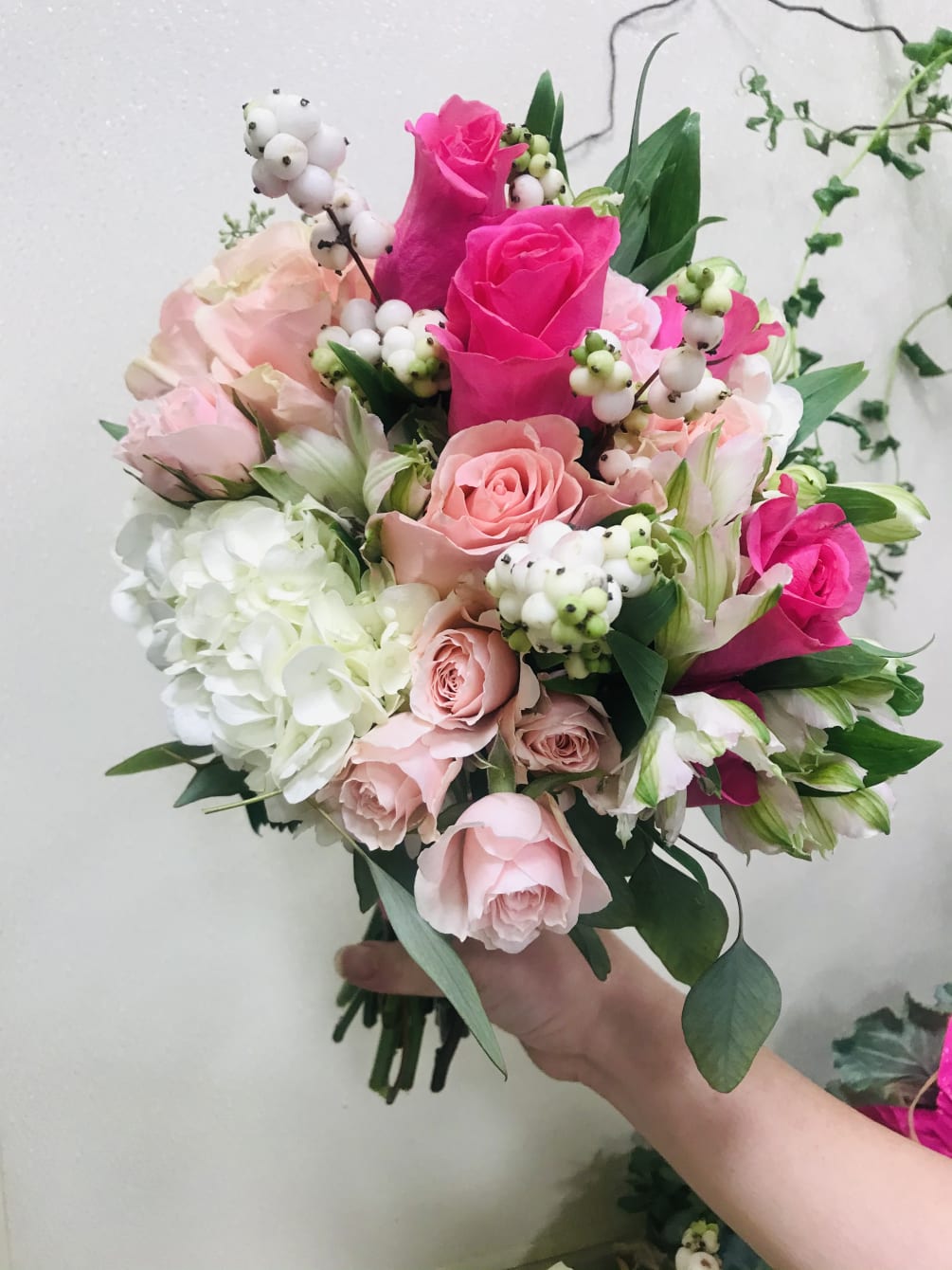 Lovely hand-tied bouquet in hot pinks roses, white hydrangea and fillers.