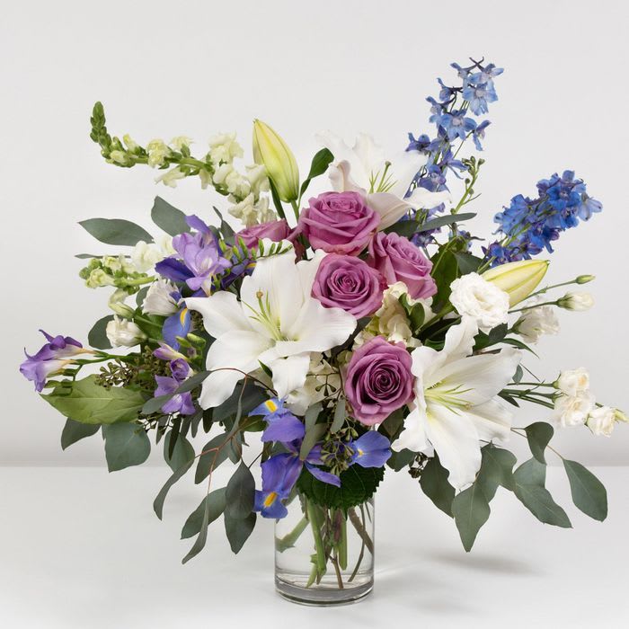 This arrangement of iris, delphinium, freesia, and asiatic lilies evokes a tranquil