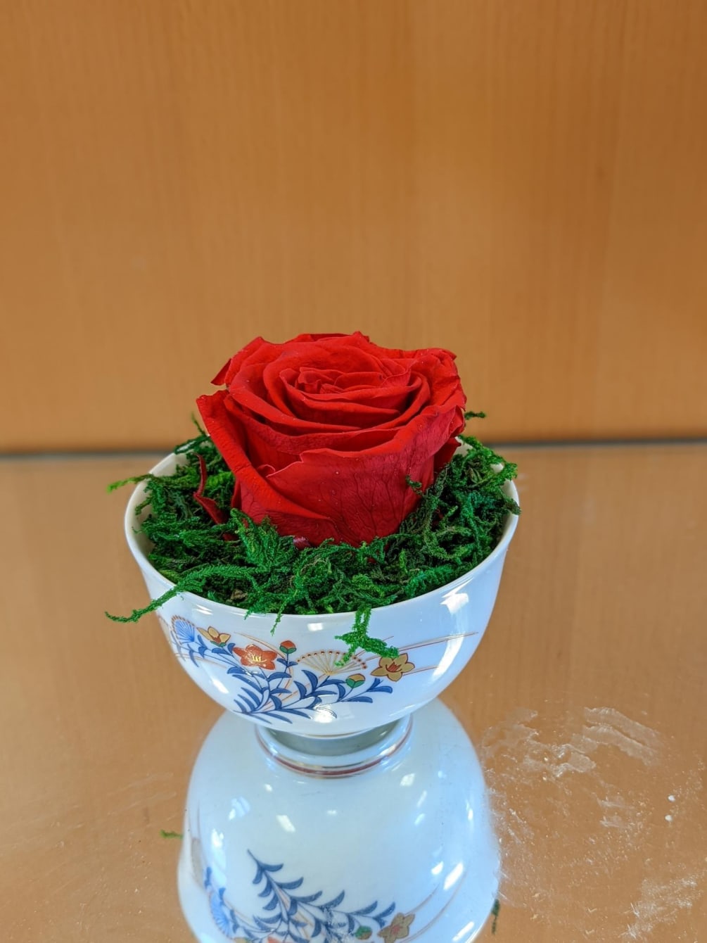 Single preserved rose artfully arranged in a teacup with moss or sand