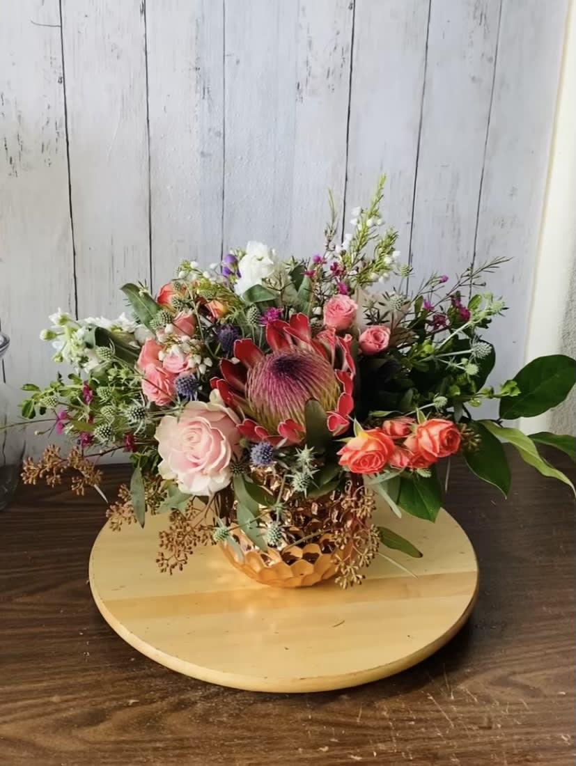 This arrangement features red/pink/orange themed flowers with a rose gold vase giving