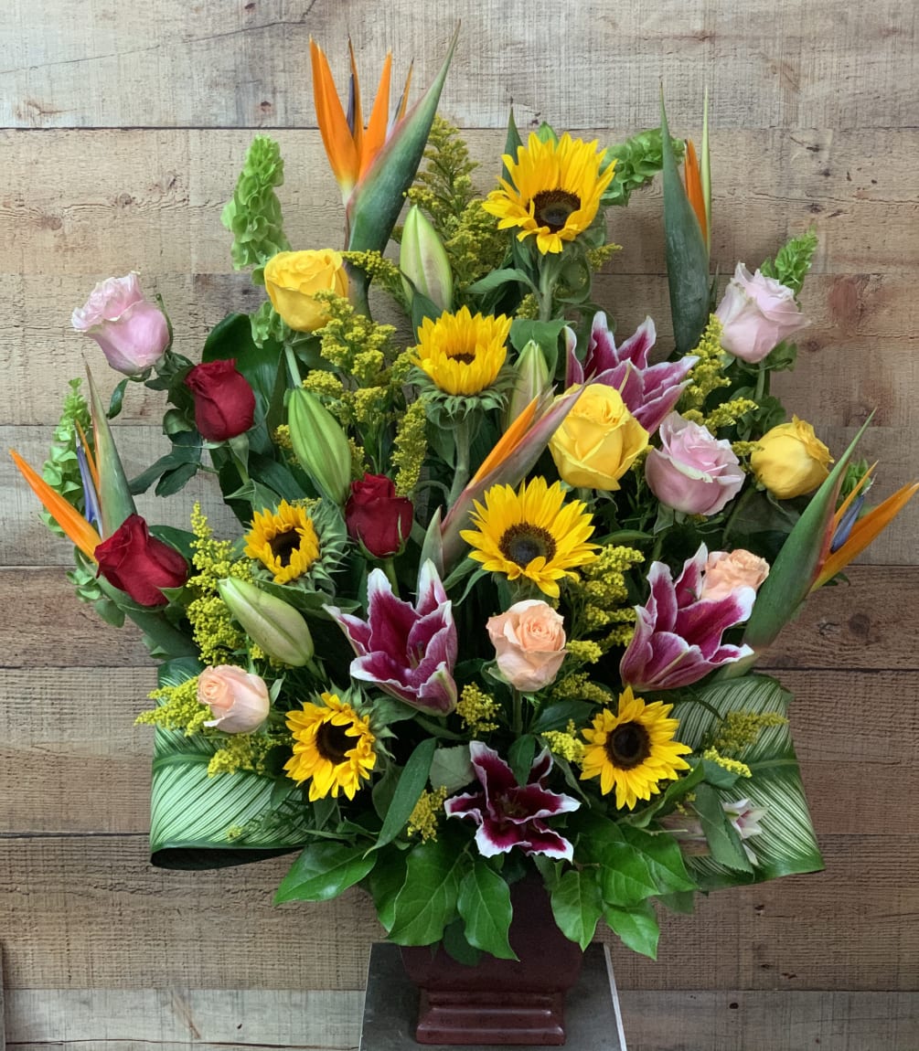 A gorgeous one sided arrangement with roses, lilies, sunflowers, and birds of