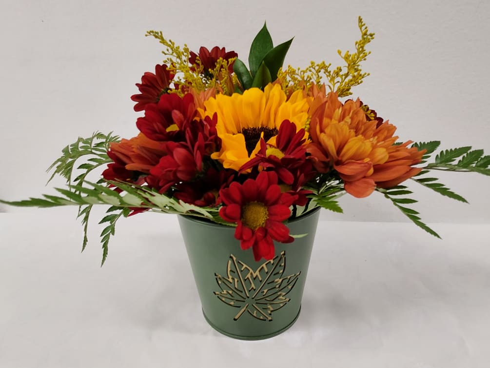 A delightful arrangement of fall toned flowers in a small green tin.