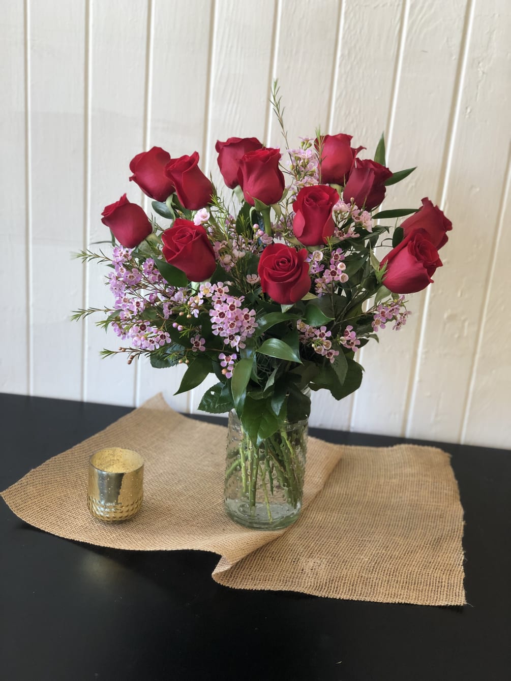 Red roses are arranged with accent flowers and greens in a clear