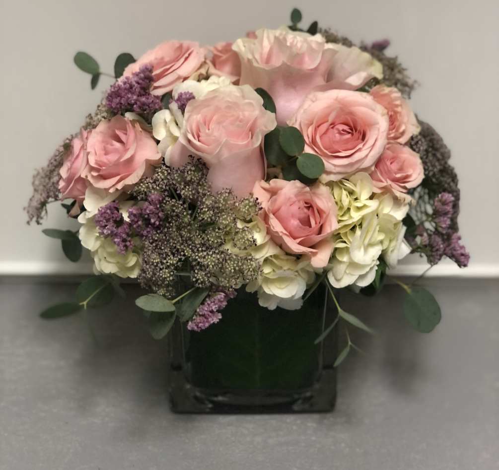 Cube vase with hydrangea, roses, and filler flowers in pink and white.