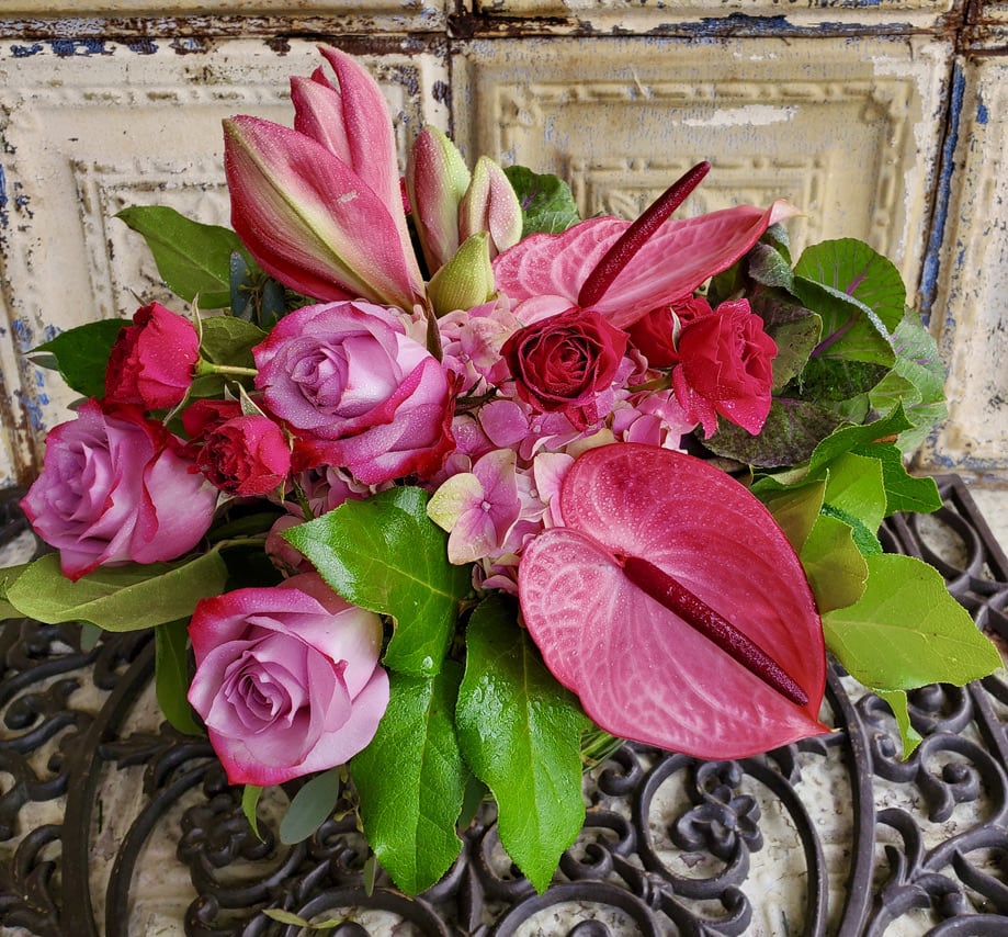 Mixed tropical arrangement with roses, spray roses, anthurium, hydrangeas, lilies, and greenery.