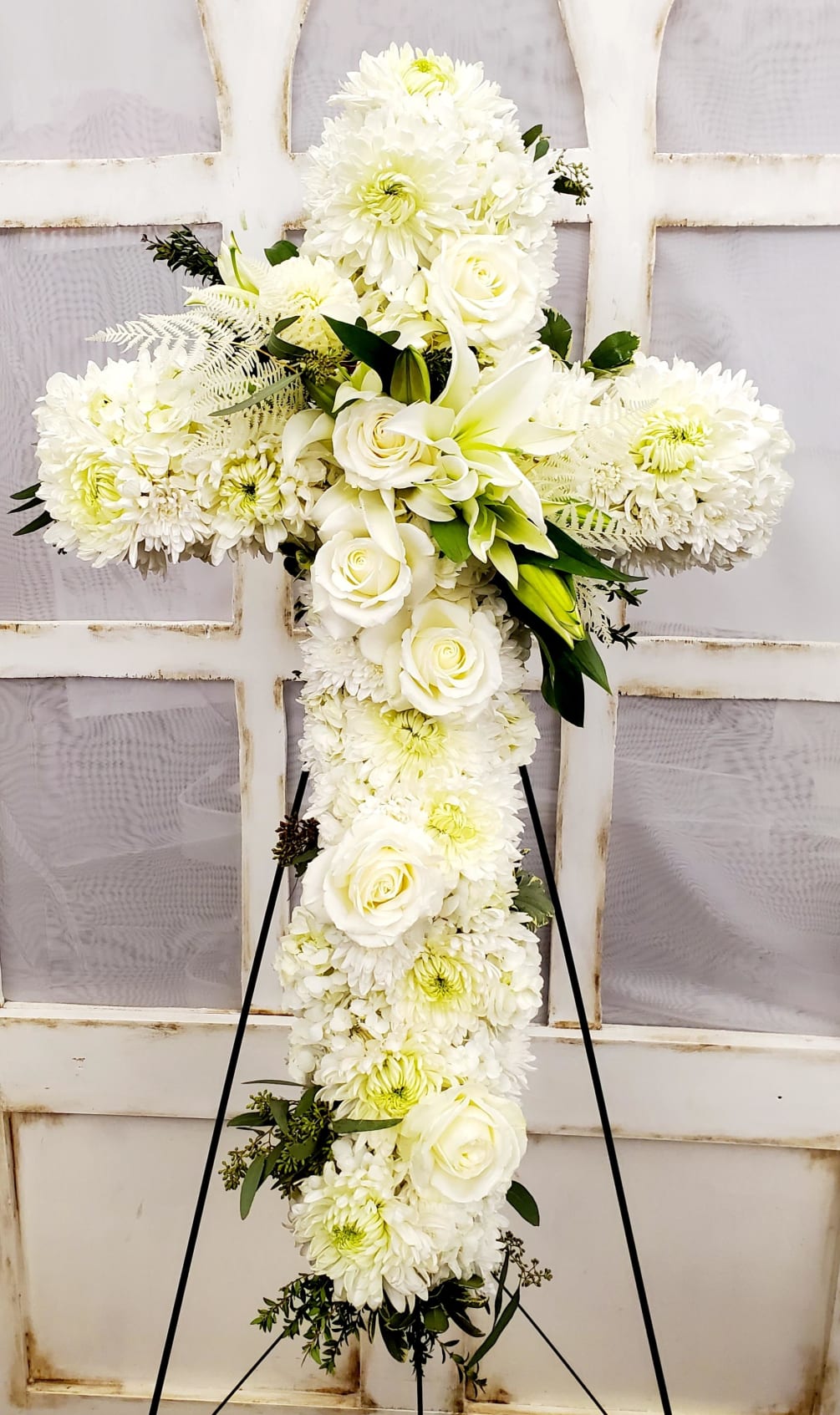 A pure white standing cross tribute created with roses, mums and lilies