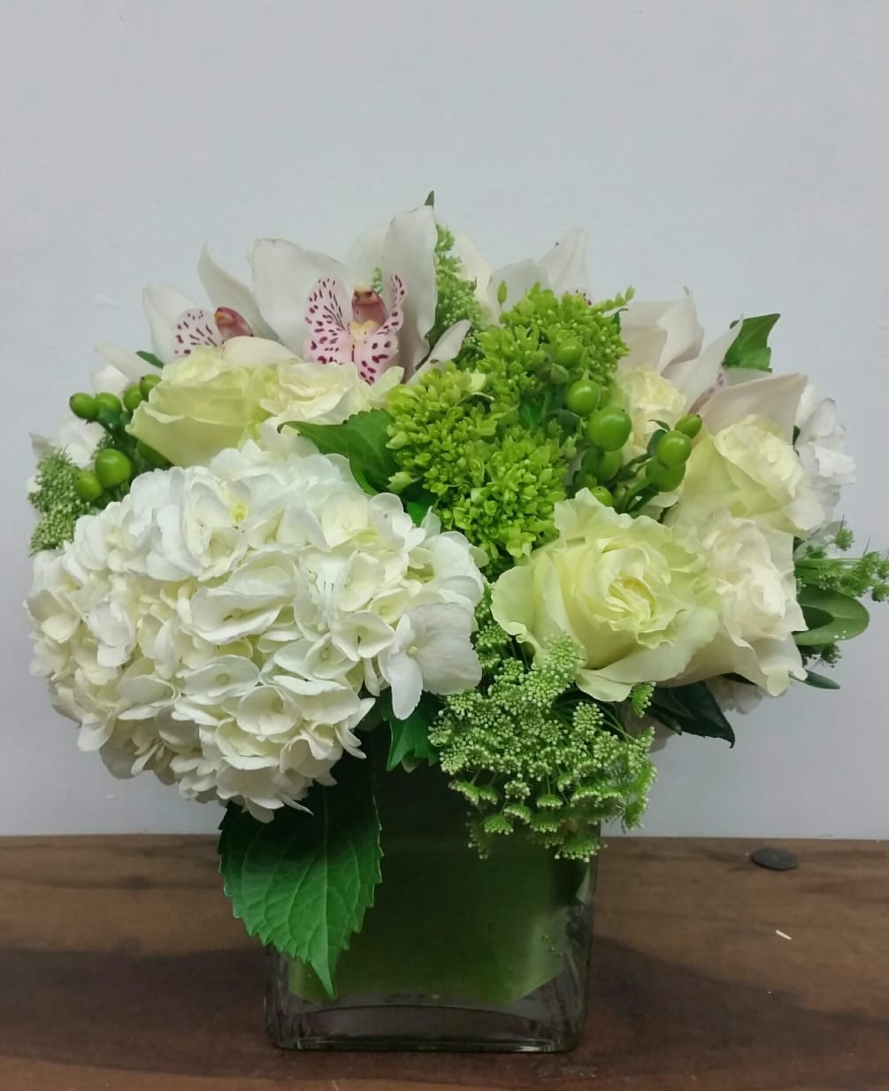 A luscious arrangement featuring cloud-like hydrangea, roses and cymbidium orchids in a