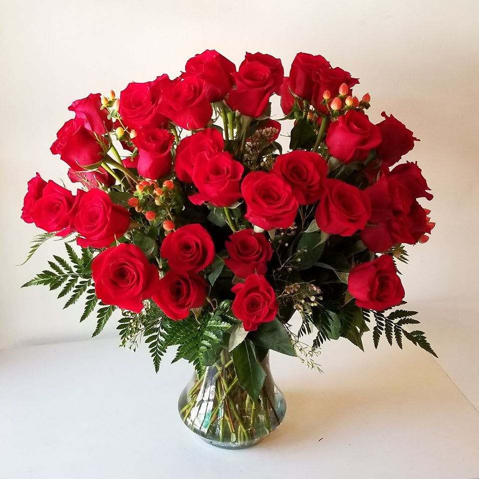 Two dozen beautiful roses are arranged with greens, wax flower and hypericum