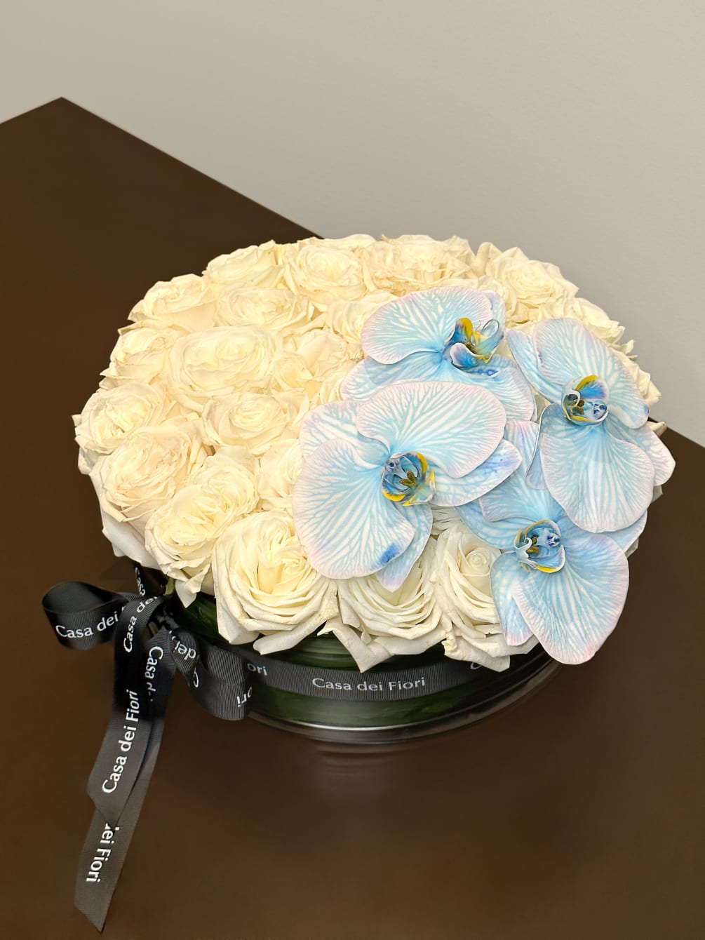 Tender white roses with cymbidium orchids arranged in a vase.
