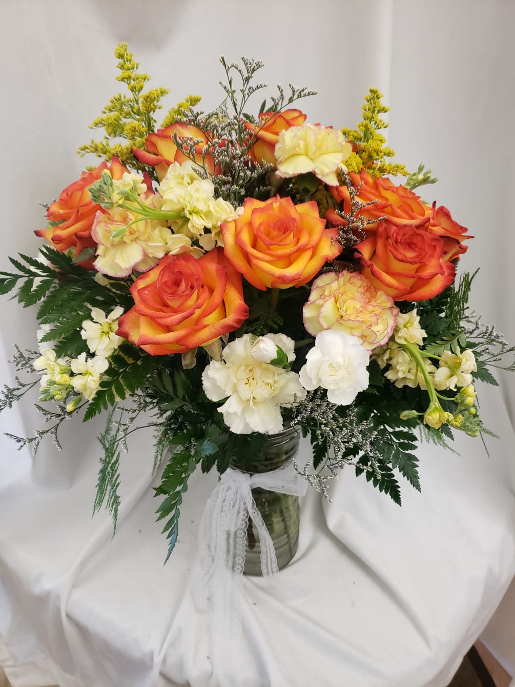 Bright and beautiful vase arrangement with vibrant orange roses, carnations, and fragrant