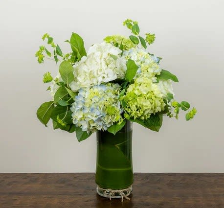 Green, white and blue hydrangea arranged in a leaf wrapped vase. Tied
