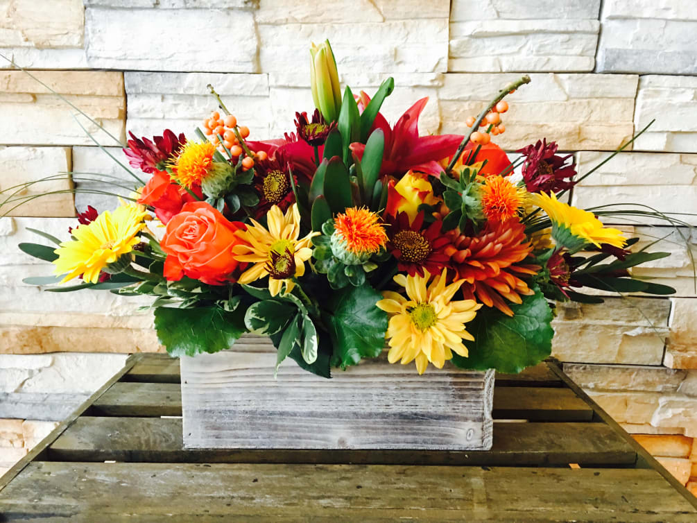 A mix of flowers in Autumn colors arrange in a wooden rectangular