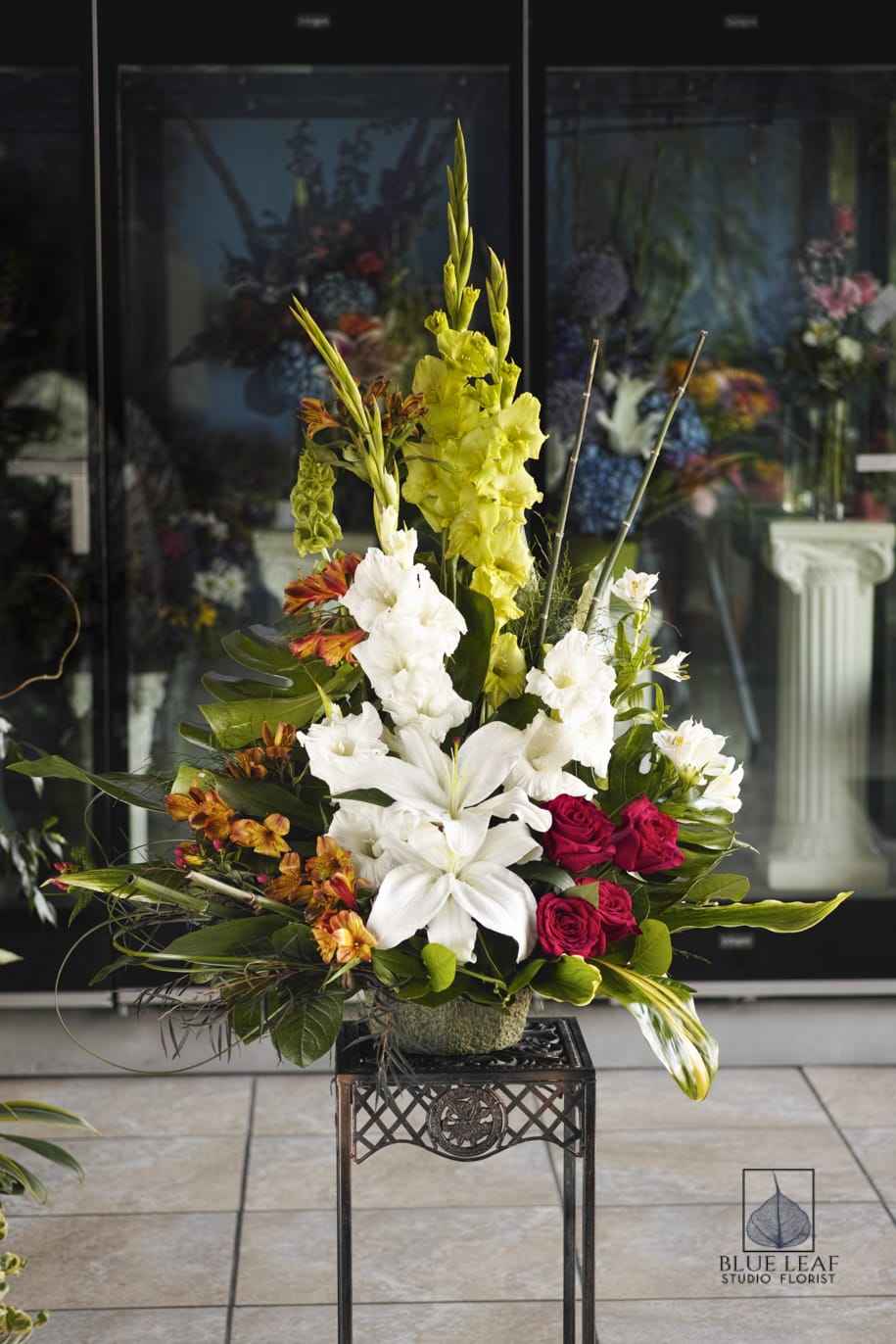 A sophisticated spray of yellow gladiolus, white lilies, spray roses, and orange