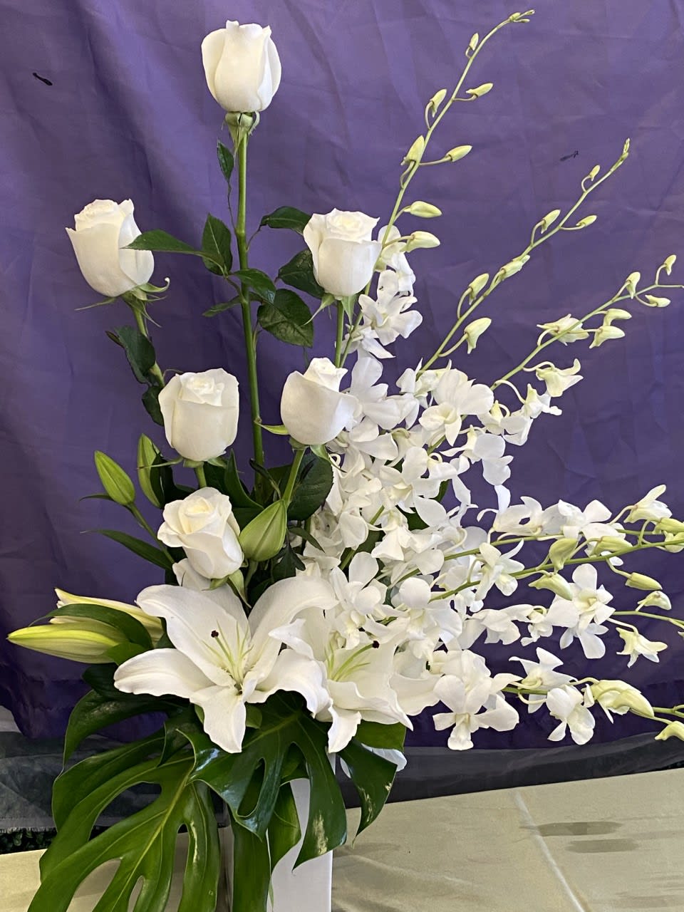 This one sided arrangement contains white Roses, Lilies, and Orchids. This arrangement