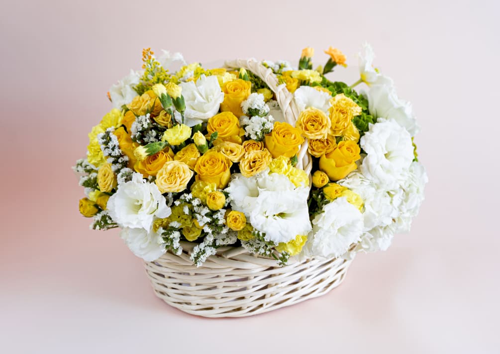 A handled white bamboo basket holds fresh elegant yellow roses, soft yellow