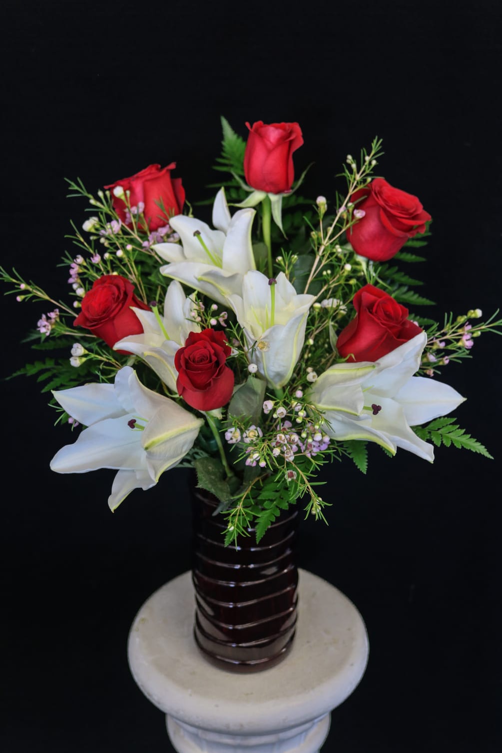 white lilies and half a dozen red roses arranged in a red