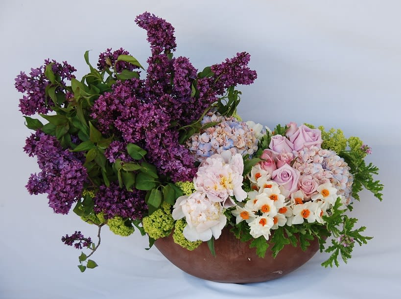 A concrete pot filled with lush lilacs, peonies, roses, viburnums, and narcissus.