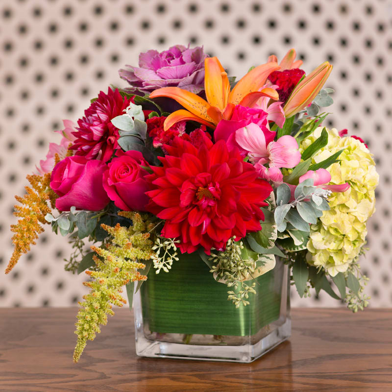 Orange Lilies, Purple Kale and Green Hydrangea in a cubed glass vase.
