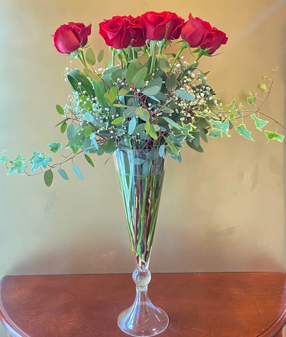 A vase full of vibrant hot pink roses, hand-arranged with ivy and