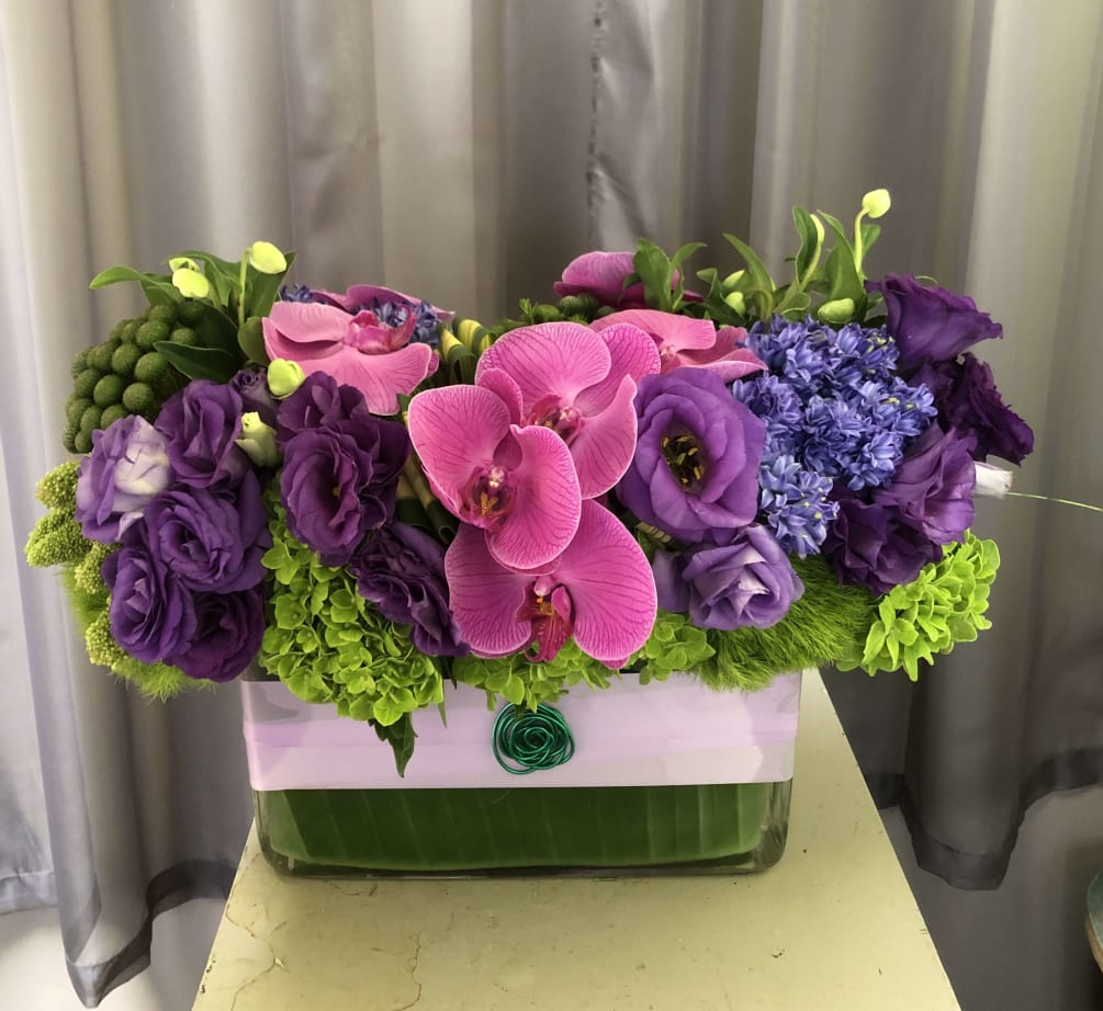 Elegant combination of different purple &amp; blue flowers in a rectangular glass