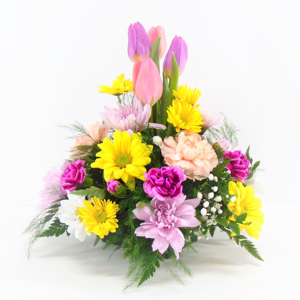 Tulips burst from a pretty pastel centerpiece of daisies, carnations and baby&#039;s