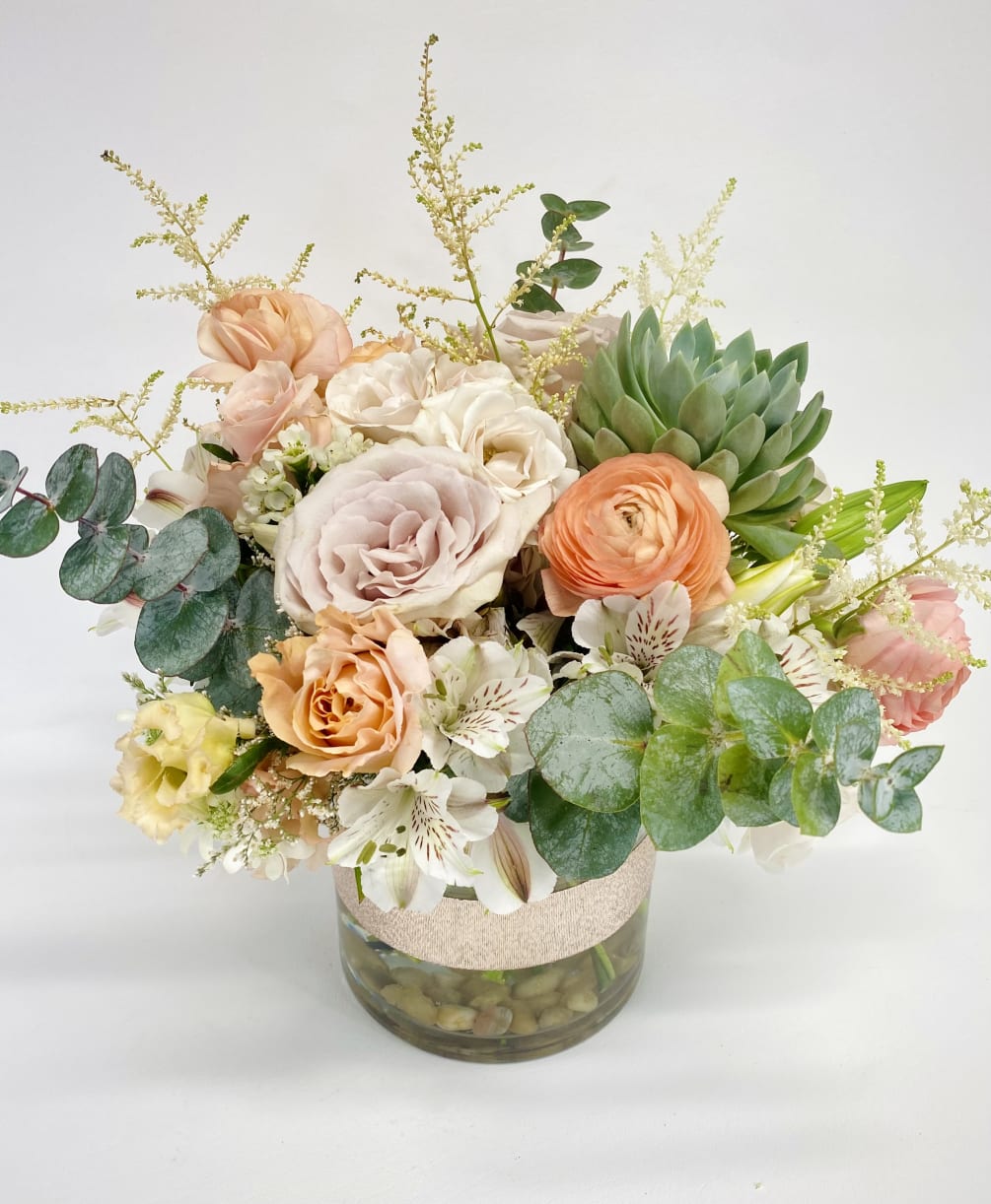 Succulent and mix of rich pastel flowers in a clear cylinder vase.