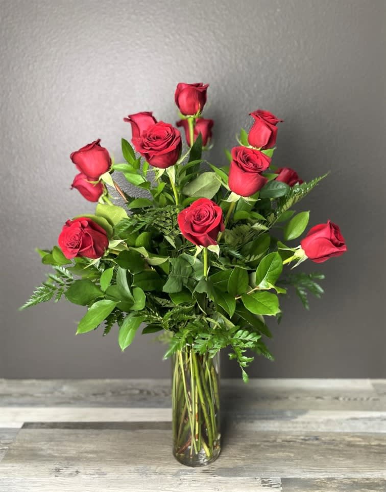 A charming bouquet of a dozen large red roses, adorned with greenery