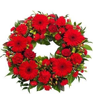 Classic red round standing wreath is designed with red gerbera daisies, red