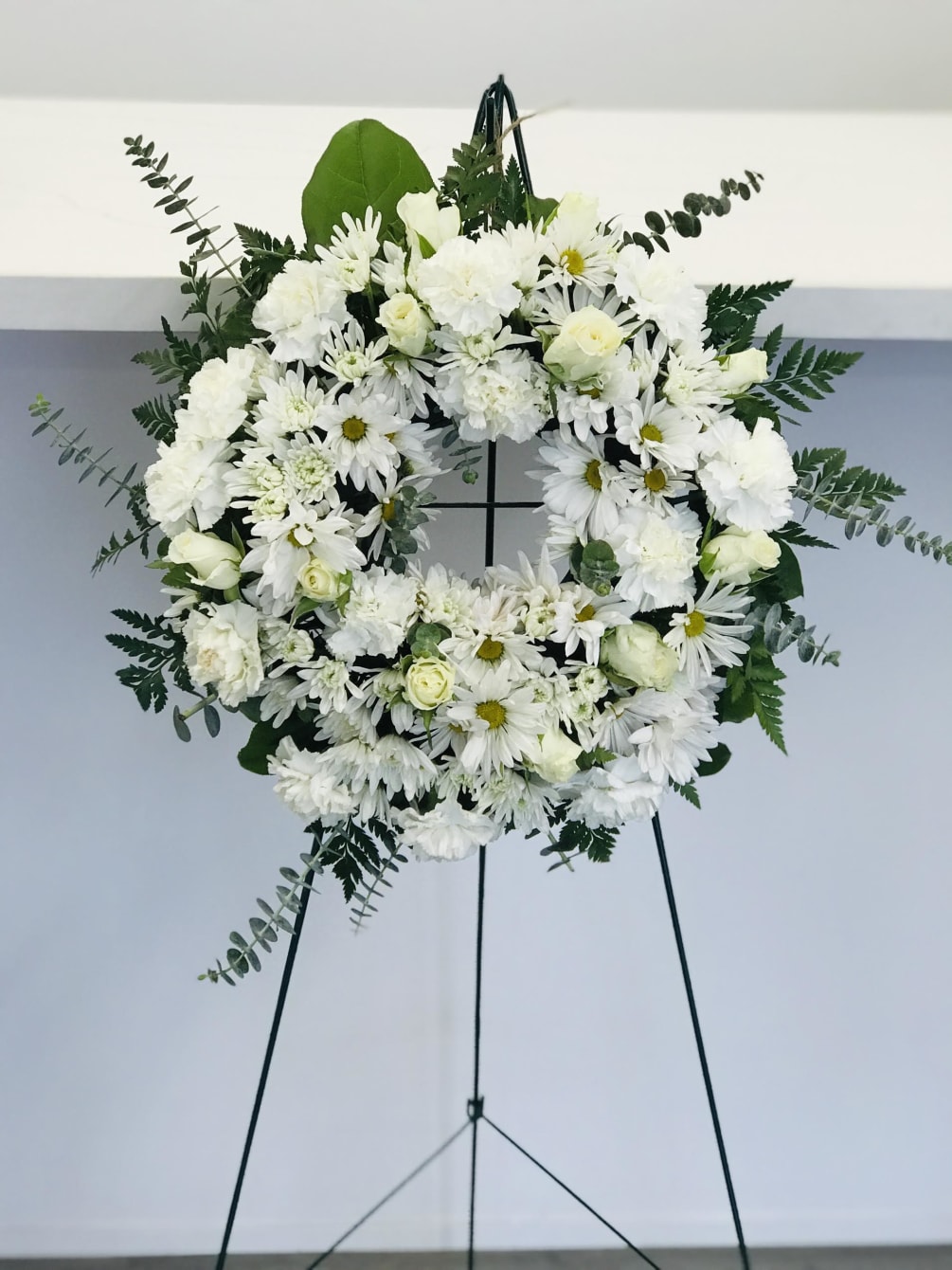Standing white wreath complete with daisies, carnations, and roses to honor the
