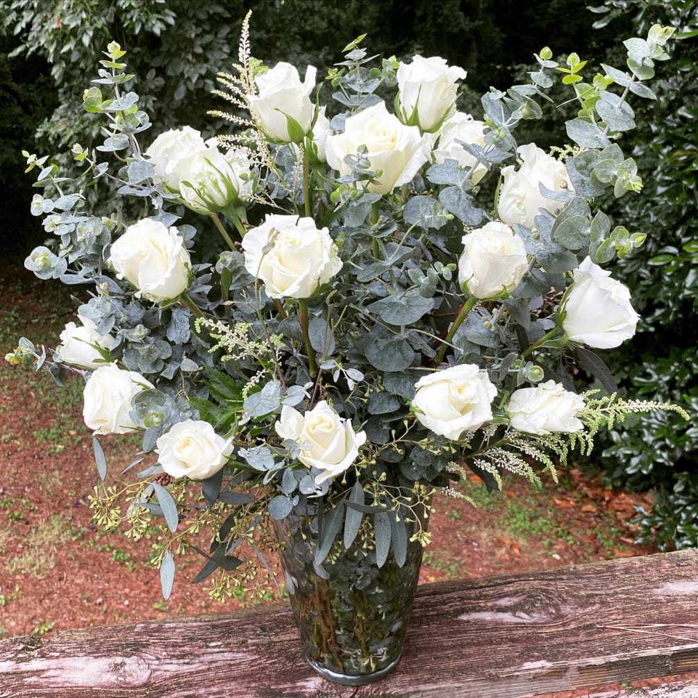 24 roses properly arranged in a vase with eucalyptus and fillers. The