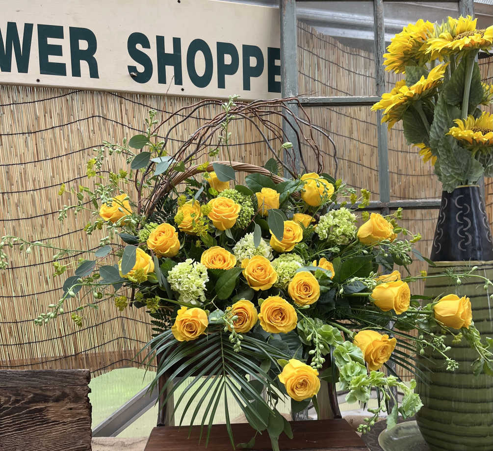 This funeral basket includes yellow roses, twigs, green hydrangea, and filler flowers
