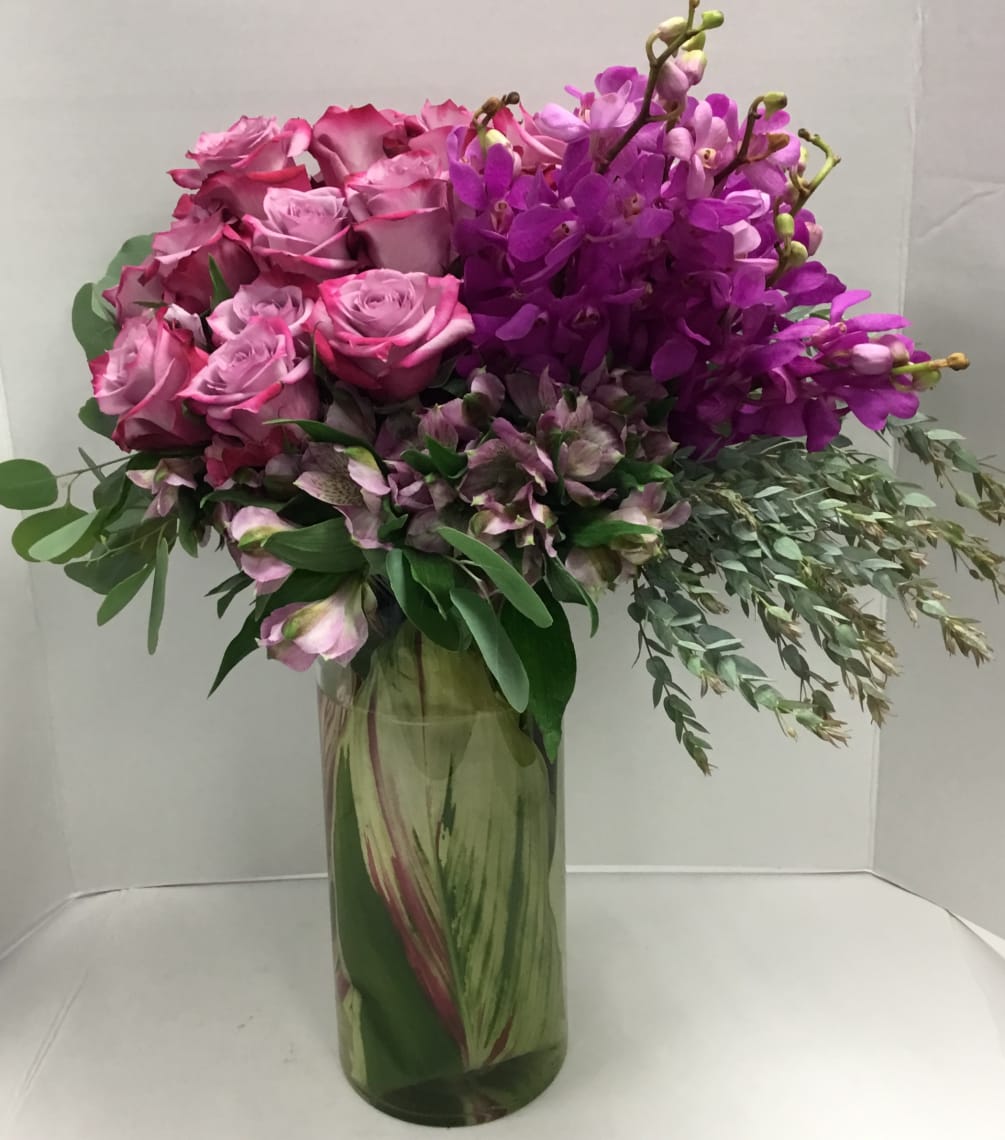 Leaf-lined vase with deep purple roses, purple orchids, purple alstroemerias and eucalyptus