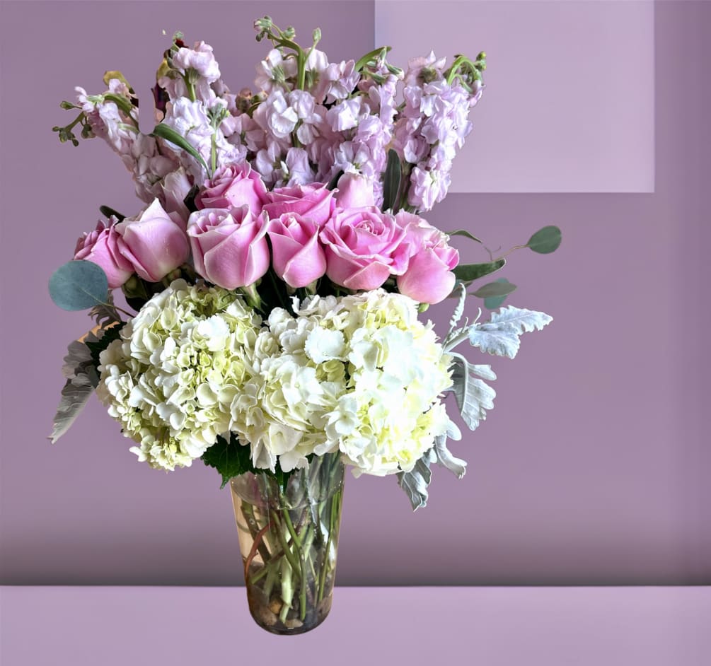 A tall arrangement of hydrangea, roses, and stock with foliage in a