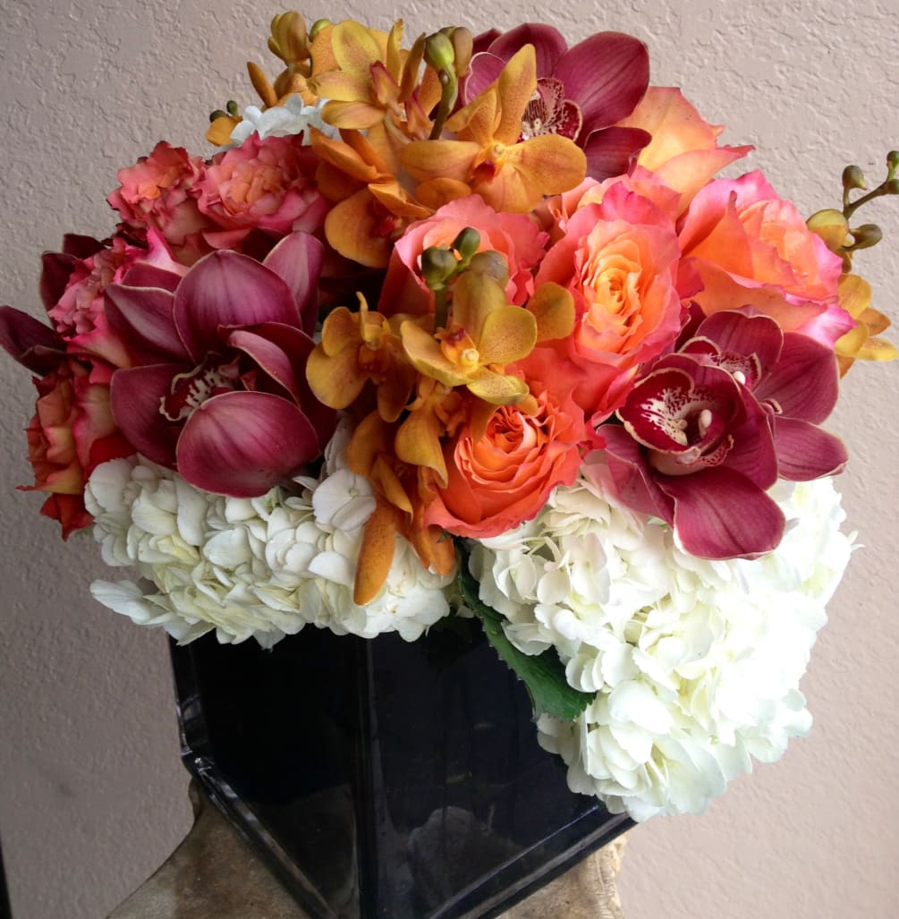 a lush treatment of orange roses, burgundy orchids in a bed of