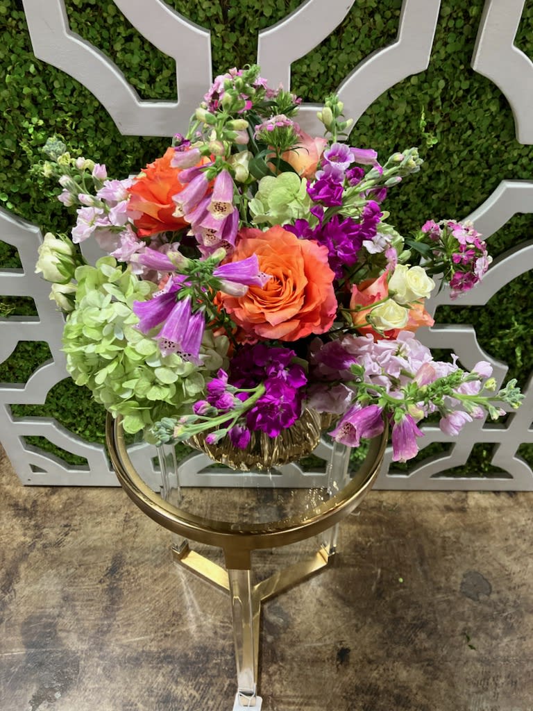 An elevated design of seasonal blooms in a unique gilded container.