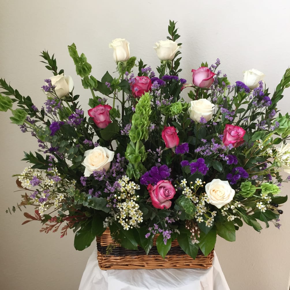 A basket of flowers include Bells of Ireland, Roses, and Greens