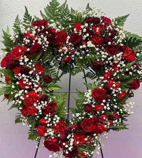 This heart shaped wreath of red roses &amp; carnations features a classic