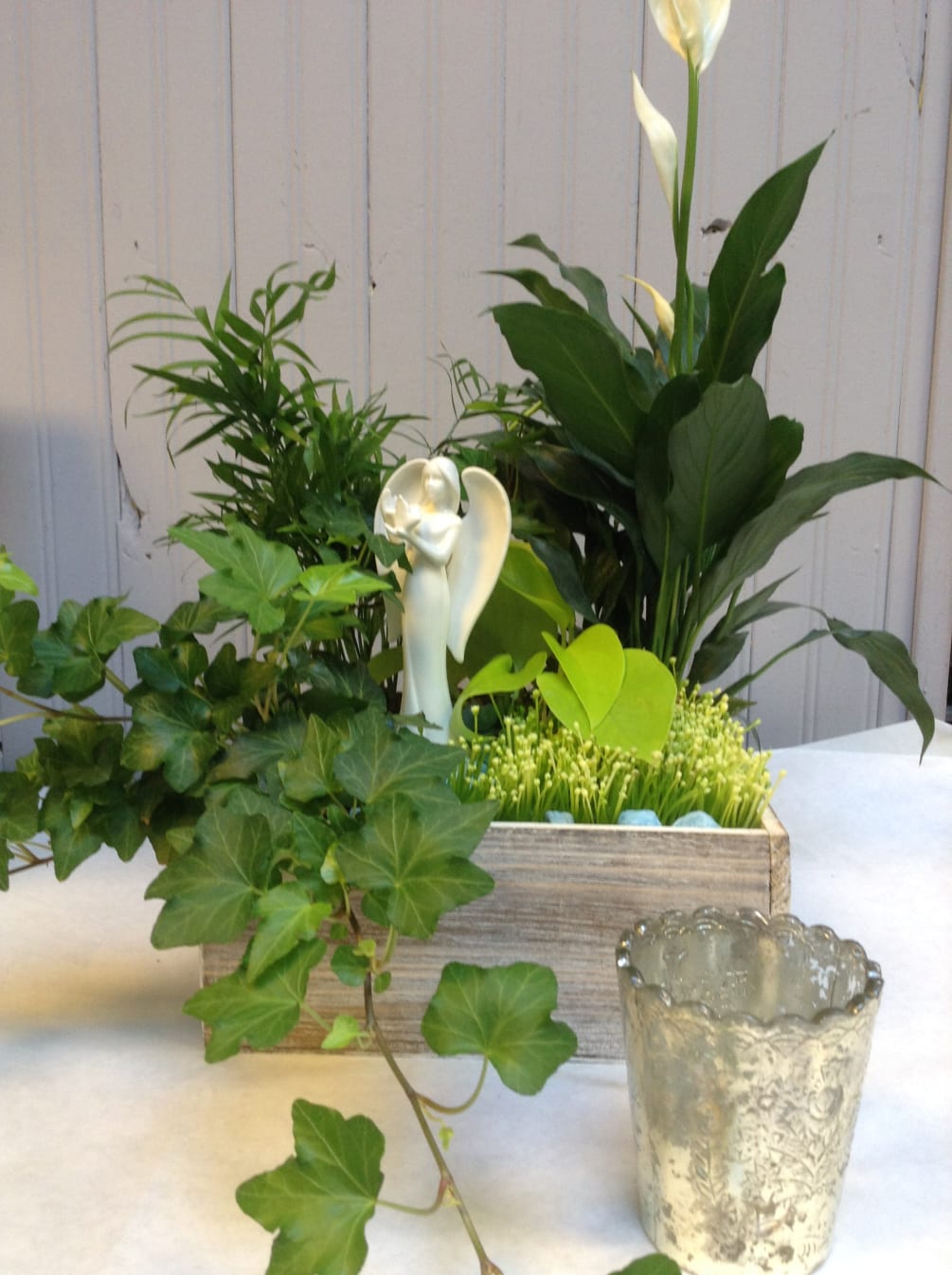 Wooden planter box with green plants and a white ceramic angel with