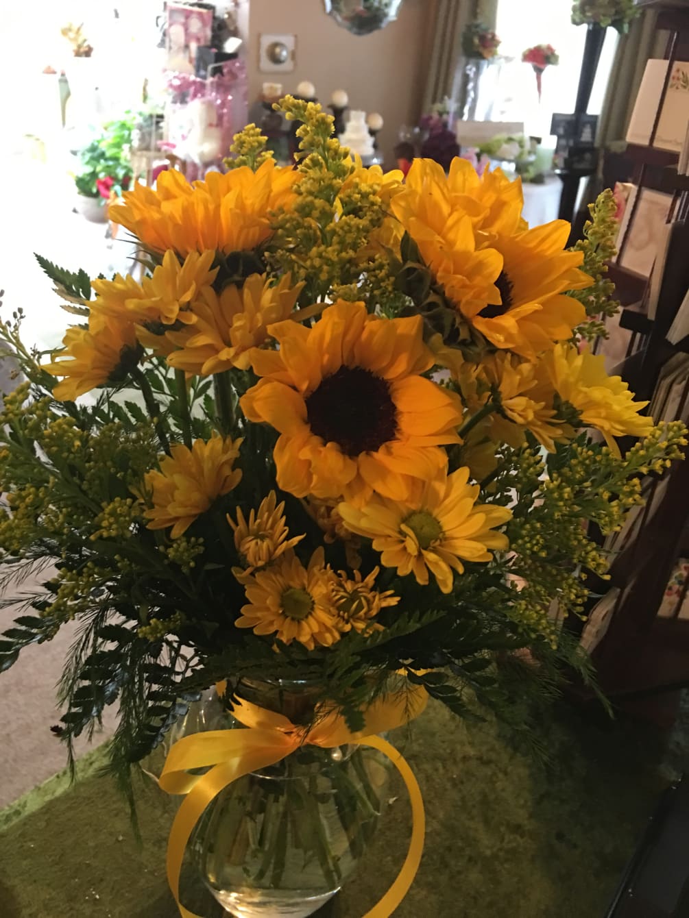Sunflowers snd yellow Daiseys adorned with yellow holler in a clear vase.