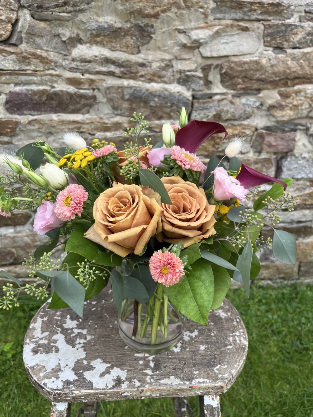 A dreamy collection of warm toffee-colored roses and plum calla lilies, accented