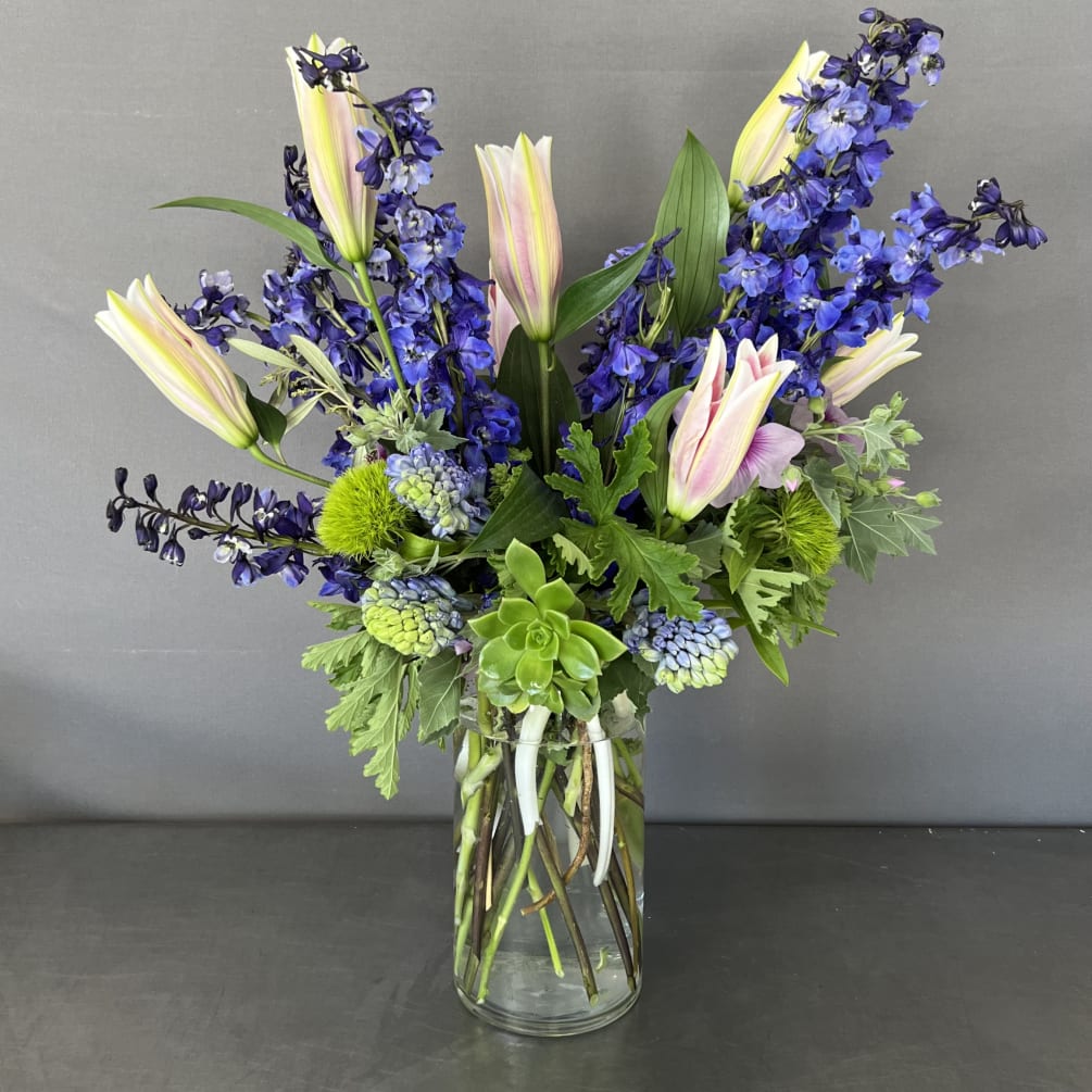 This floral piece has blue delphinium flowers combined with oriental lilies and