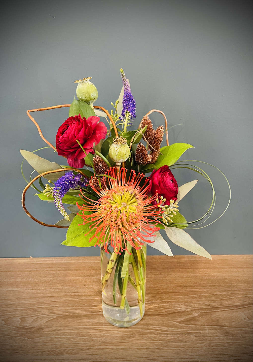 A funky mix of pink cushion protea, ranunculus, poppy pods, veronica and