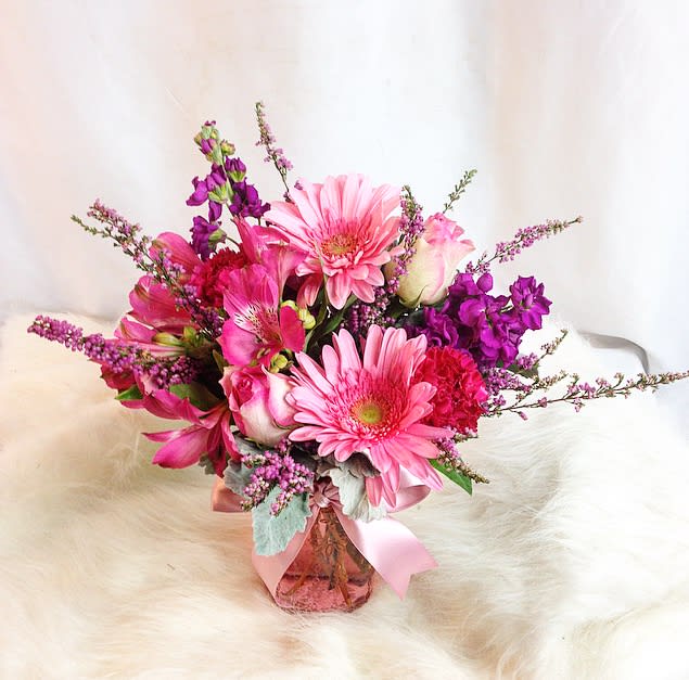 In a pink mason jar, a mixture of all pink flowers including