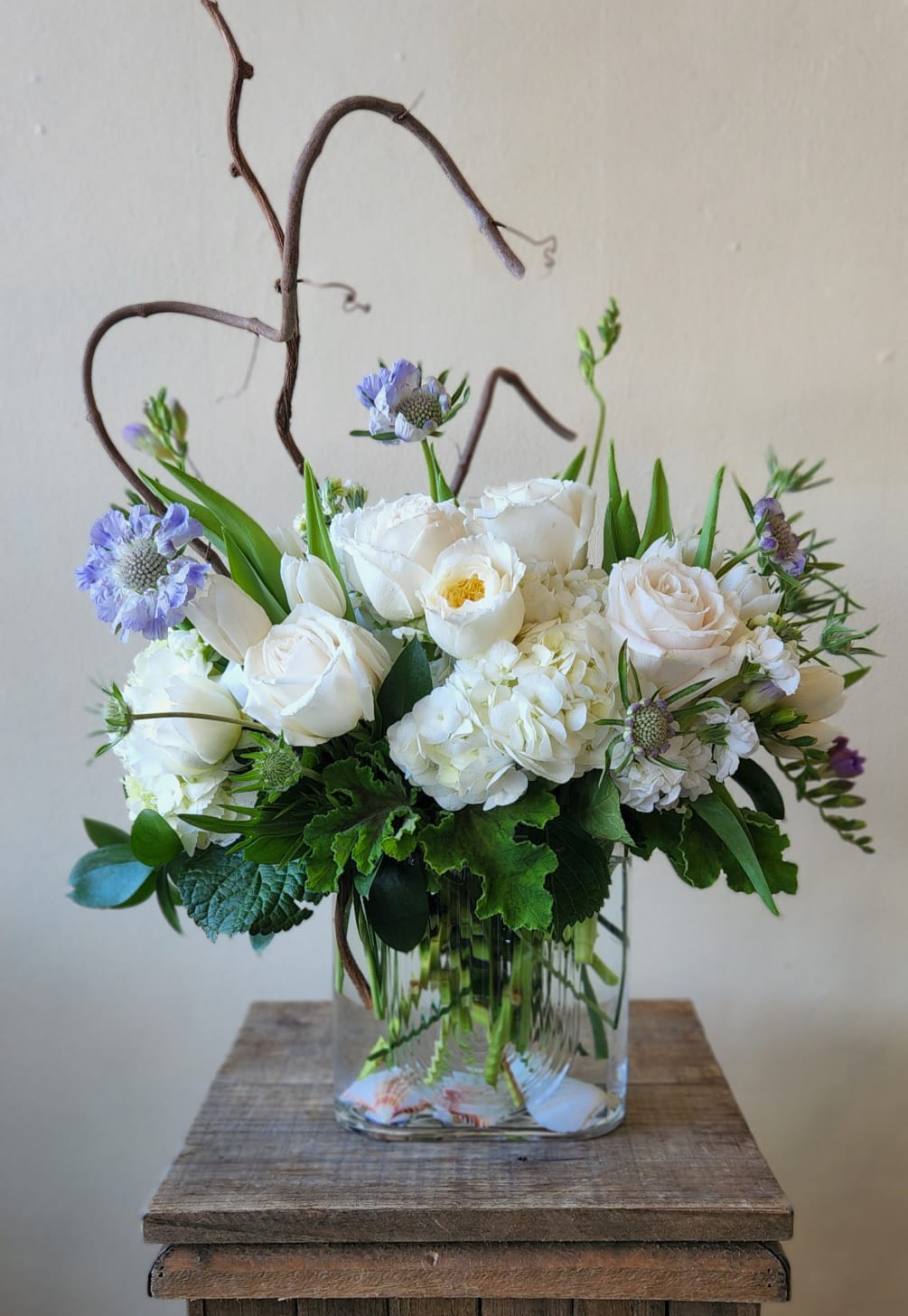 A coastal inspired arrangement of roses, hydrangea, and lisianthus with branch and