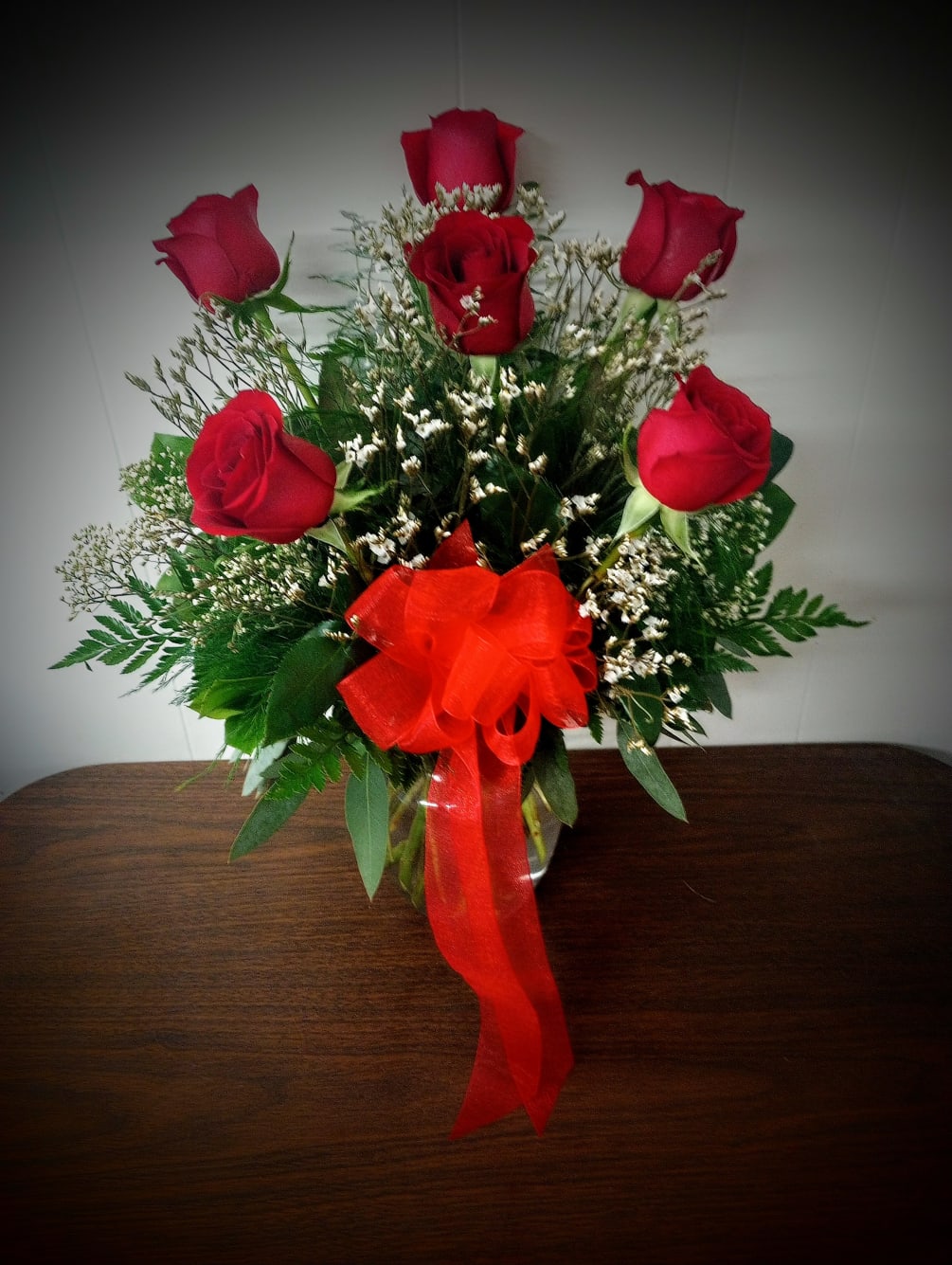Six red roses arranged in a vase and beautifully trimmed with filler