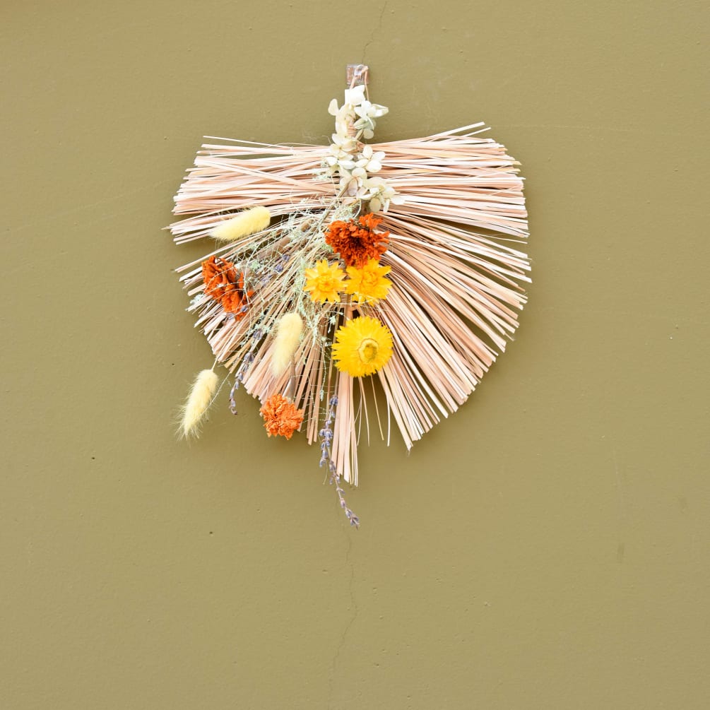 A unique handmade palm-shaped wreath made out of straw. Preserved flowers have