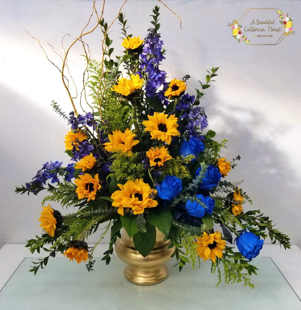 Uplifting sunflowers and royal blue roses spring forth from a golden urn.