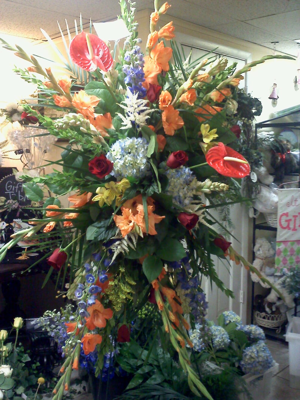 this colorful standing funeral spray has an assortment of red anthuriums, orange