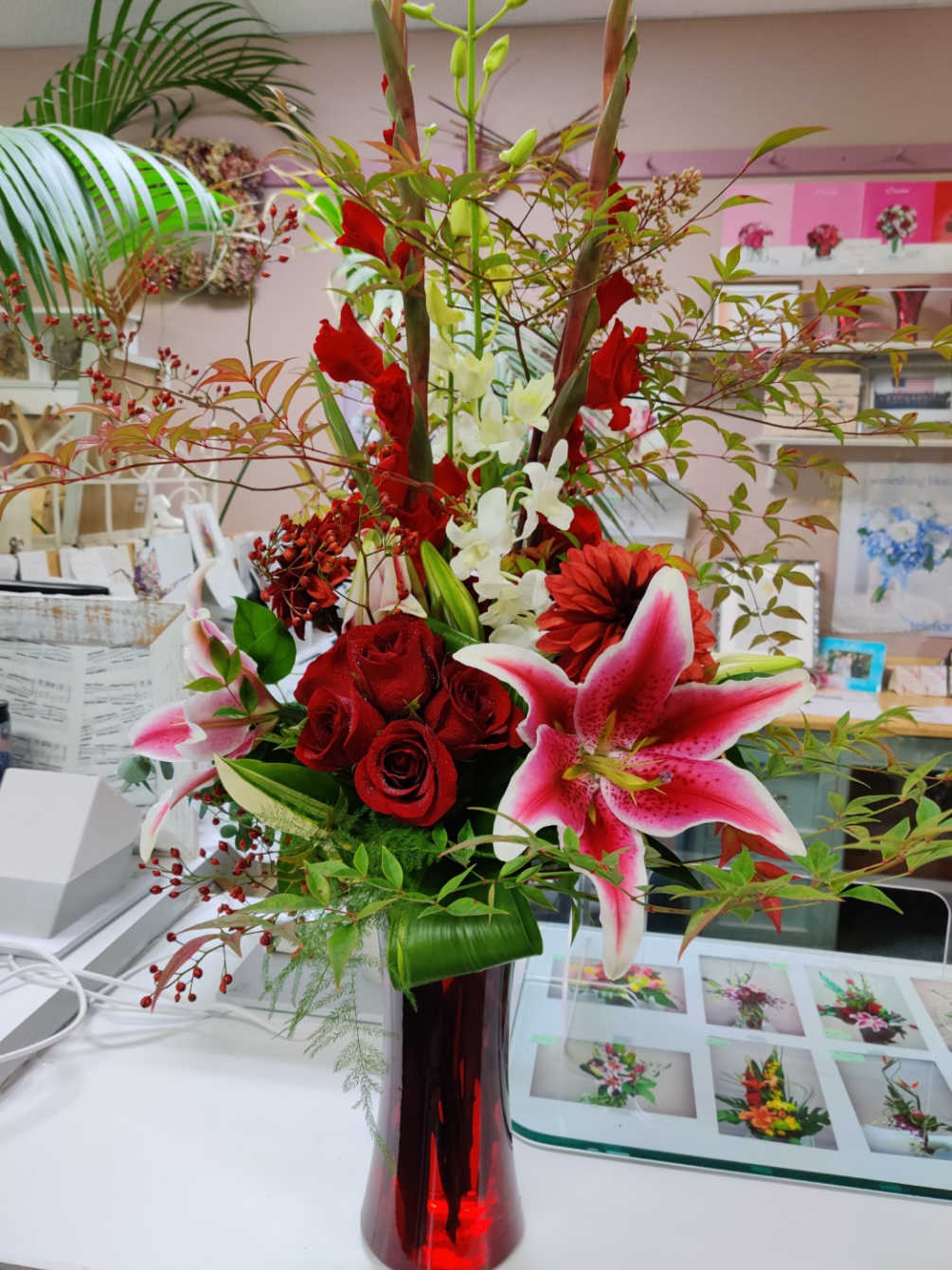 Contains Gladiolus, Orchids, Roses, Stargazer, Dahlia, Cox in a Tall Red Vase