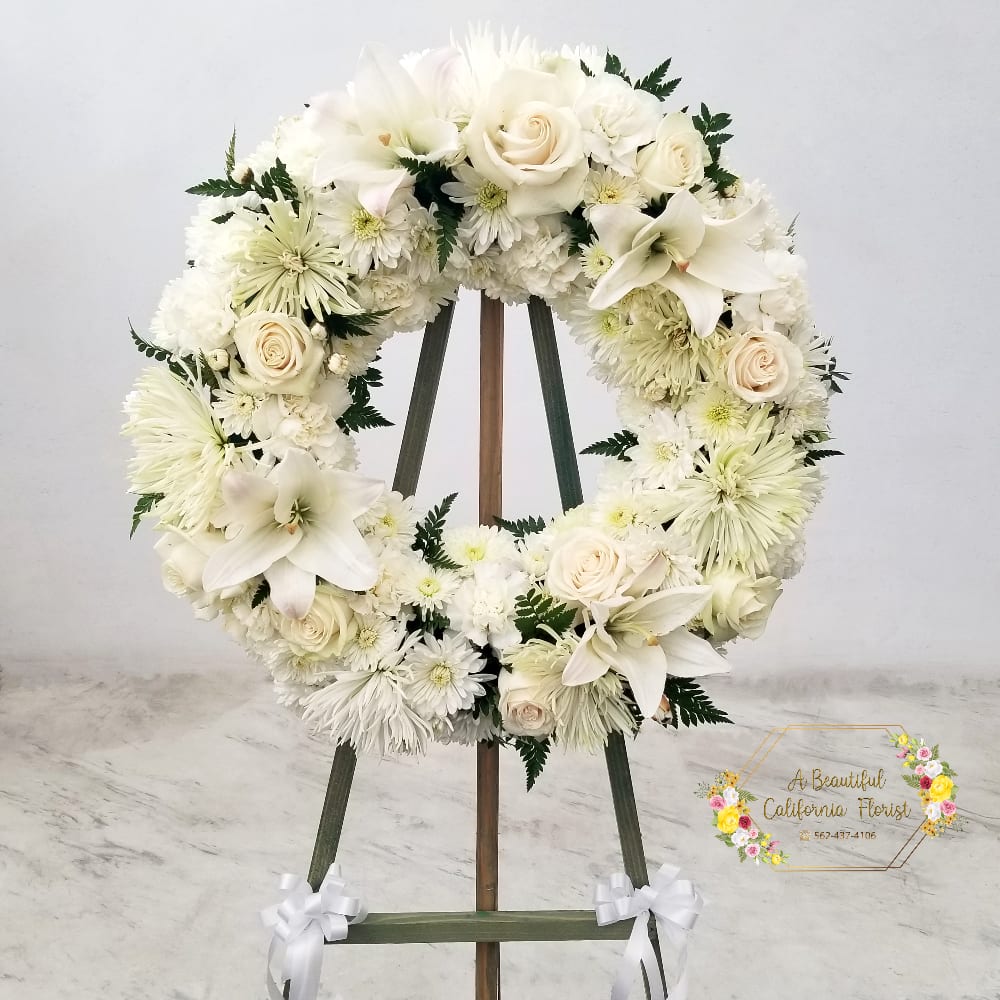 Beautiful sympathy wreath of white roses, lilies, mums and carnations. Accented by